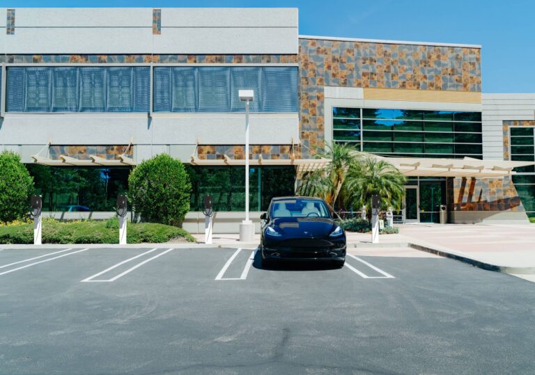 tesla backed into charging slot at ev station with modern office building in background