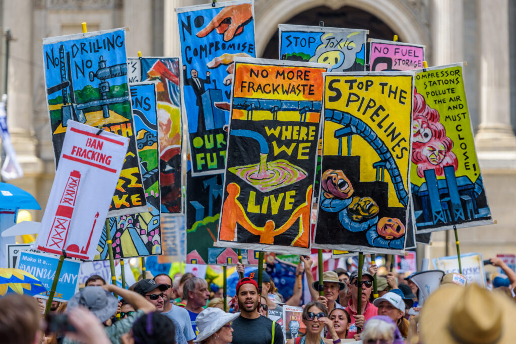 With Independence Hall in the background, a crowd of people hold signs with messages including 