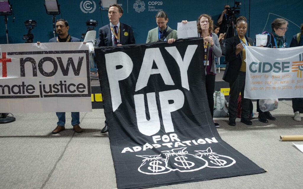 Protestors at COP29 hold a sign that says "Pay Up for Adaptation"