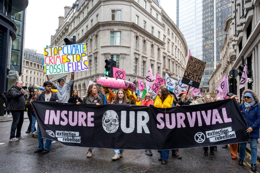 Several hundred activists marched through the streets of London on Oct. 28, holding flags bearing the Extinction Rebellion logo and posters calling for insurance companies to stop underwriting fossil fuel projects. Credit: Keerti Gopal/Inside Climate News