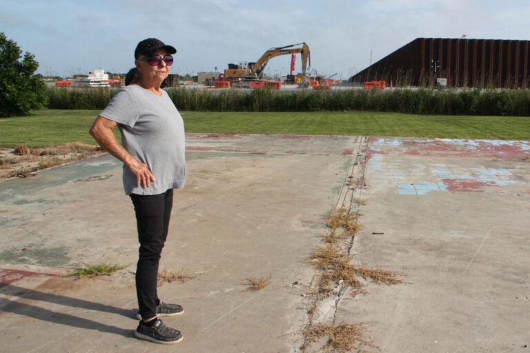 Sherry Peshoff stands on a slab where a home use to sit next to the perimeter wall of Venture Global’s CP2 terminal in Cameron, La. Credit: Nicholas Kusnetz/Inside Climate News