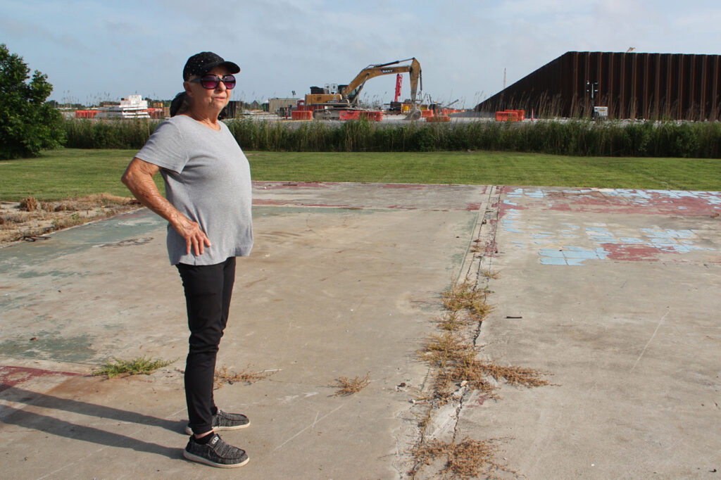 Sherry Peshoff stands on a slab where a home use to sit next to the perimeter wall of Venture Global’s CP2 terminal in Cameron, La. Credit: Nicholas Kusnetz/Inside Climate News