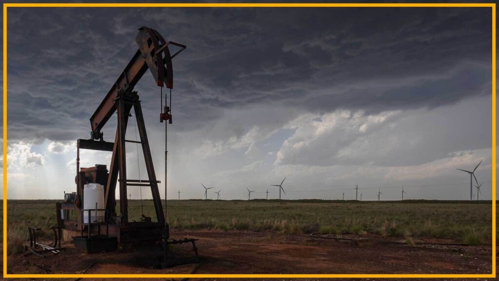 A close up of an oil rig with wind turbines in the background.