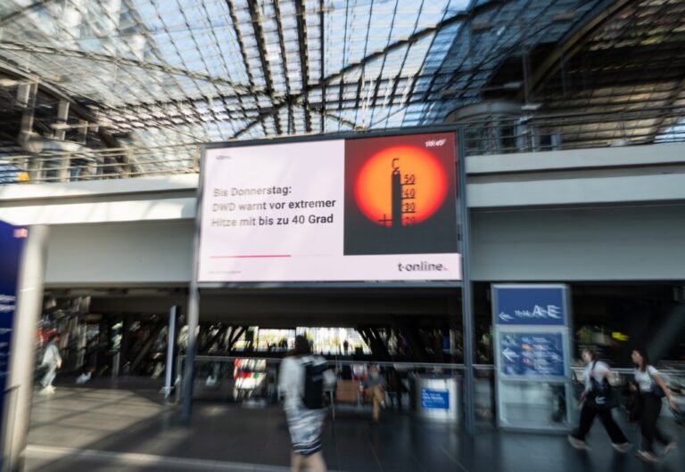 Passengers walk past a heat-warning display at the main train station in Berlin, Germany